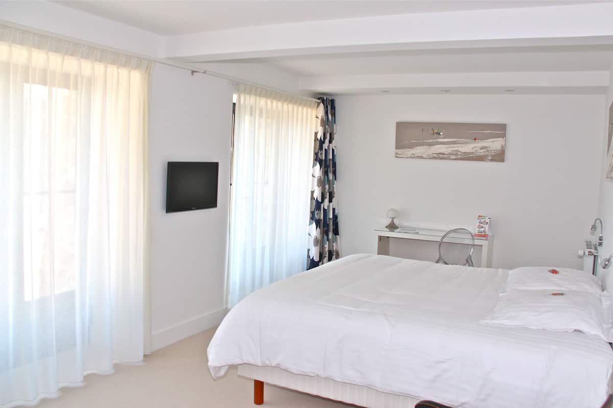A bedroom with a large bed, a bedside table, a TV mounted on the wall, and a window with curtains.