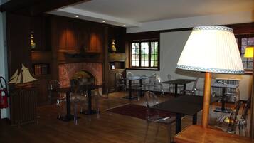 A spacious living area with a fireplace, wooden flooring, and clear plastic chairs.