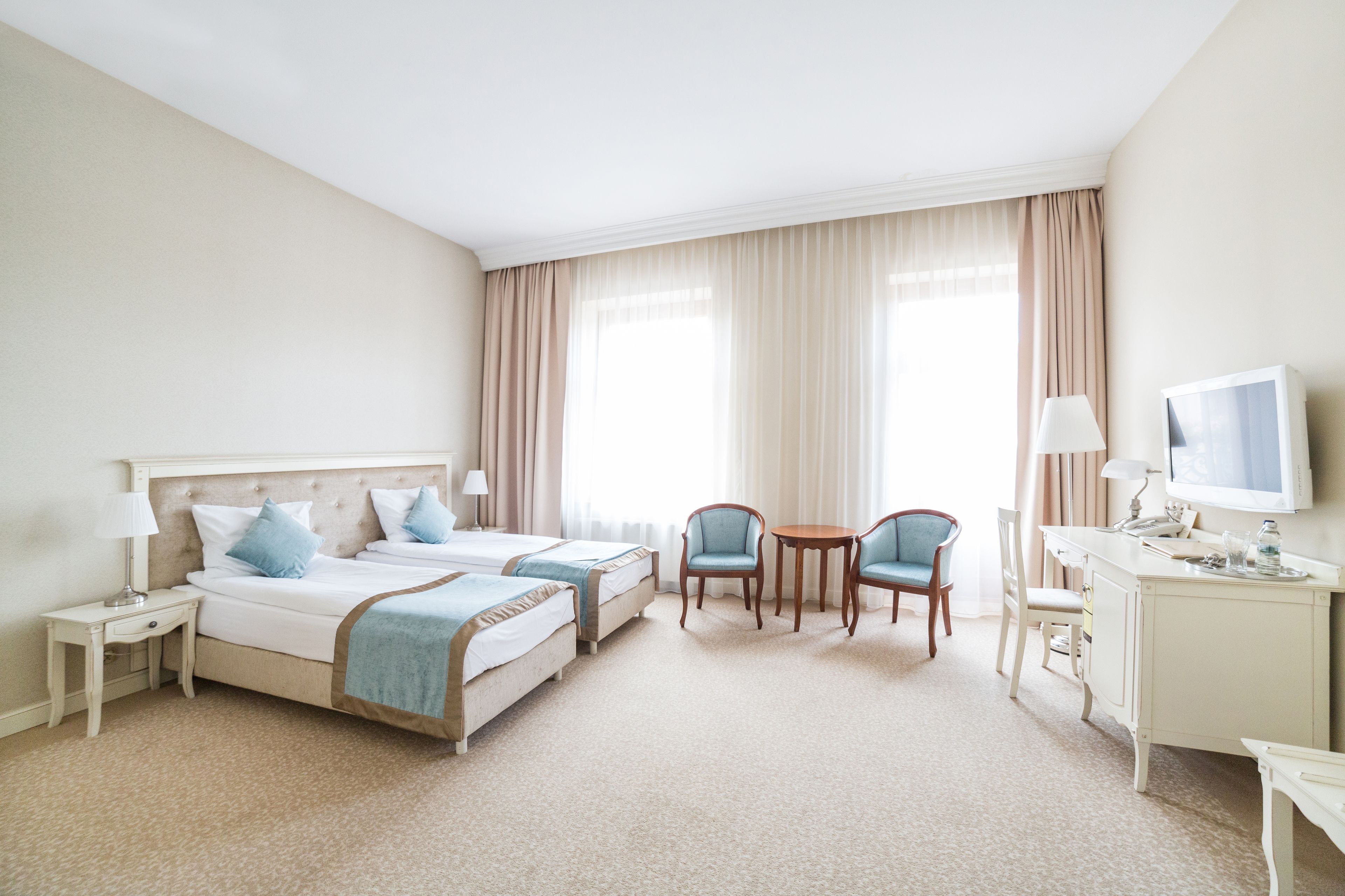 A hotel room with two beds, a desk, a chair, and a television.