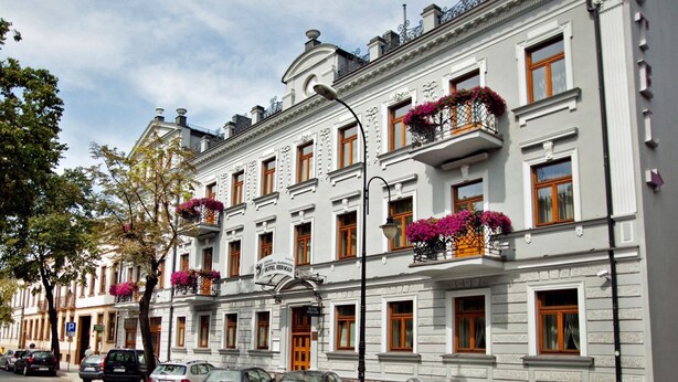 Un hôtel à plusieurs étages, doté de balcons ornés de jardinières fleuries, d’un style architectural classique et surplombant un ciel dégagé.