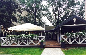 A covered outdoor area with string lights, white lattice railings, and potted plants.