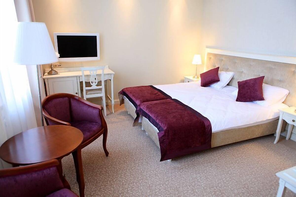 A hotel room with a large bed, a desk with a computer, a chair, and a small table.