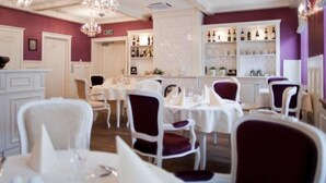 Un restaurant avec des tables et des chaises blanches, un bar avec des étagères remplies de bouteilles et un lustre.