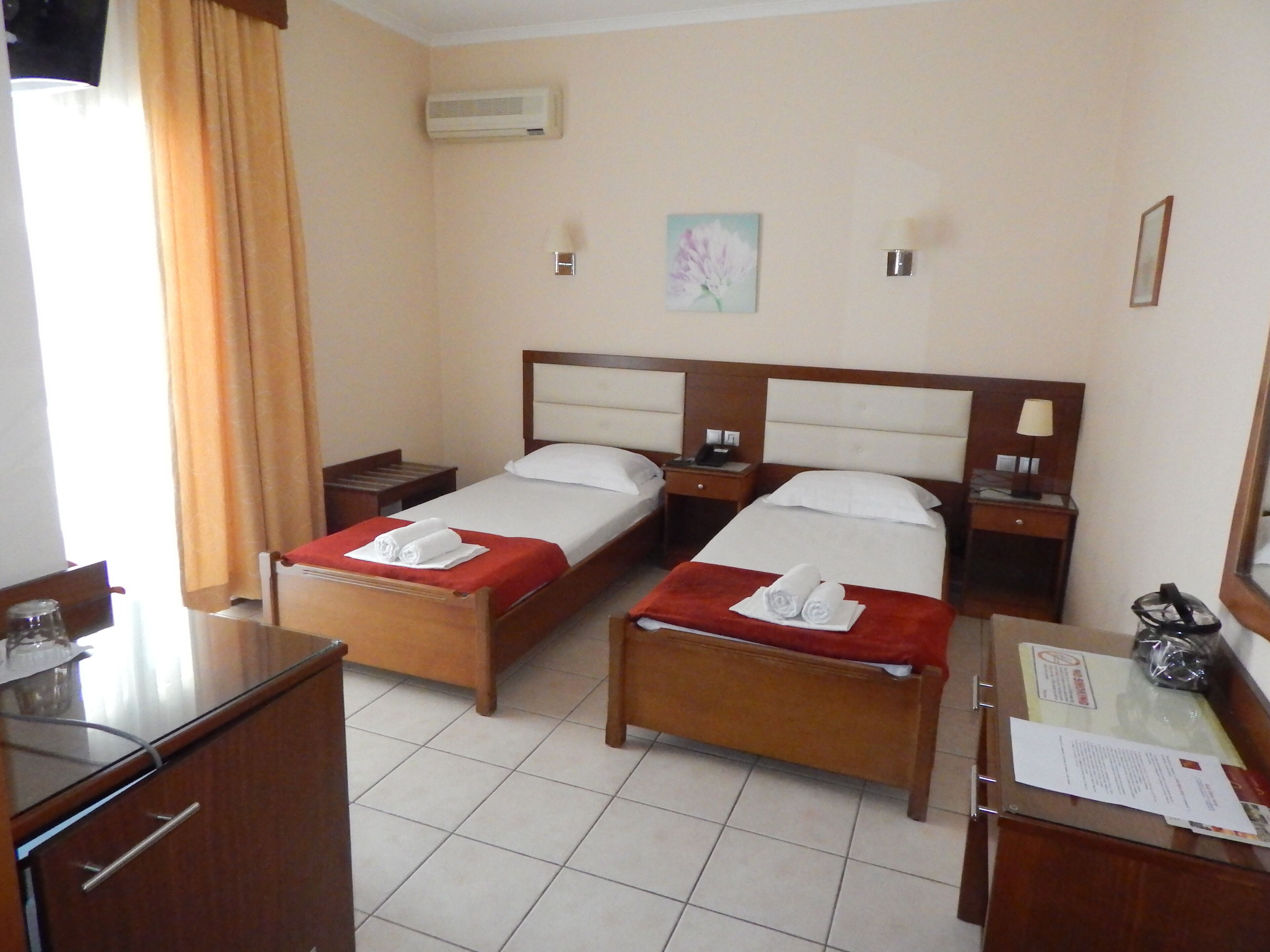 A hotel room with two beds, a desk, a chair, a mirror, and a window with curtains.
