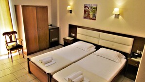 Habitación de hotel con dos camas, una silla, un armario y una mesita de noche.