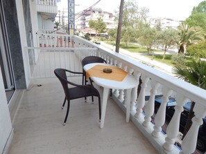 Un balcón con barandilla blanca, una mesa con dos sillas y vistas a una zona residencial con árboles y edificios.