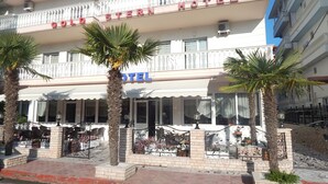 Un hotel con balcón, palmeras y mobiliario exterior.