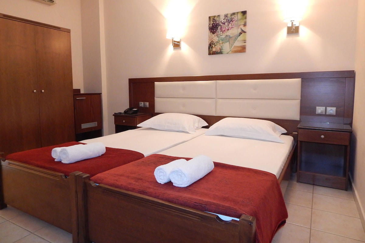 Una cama doble con dos almohadas, cabecera de madera, mesita de noche con teléfono y lámpara de pared.