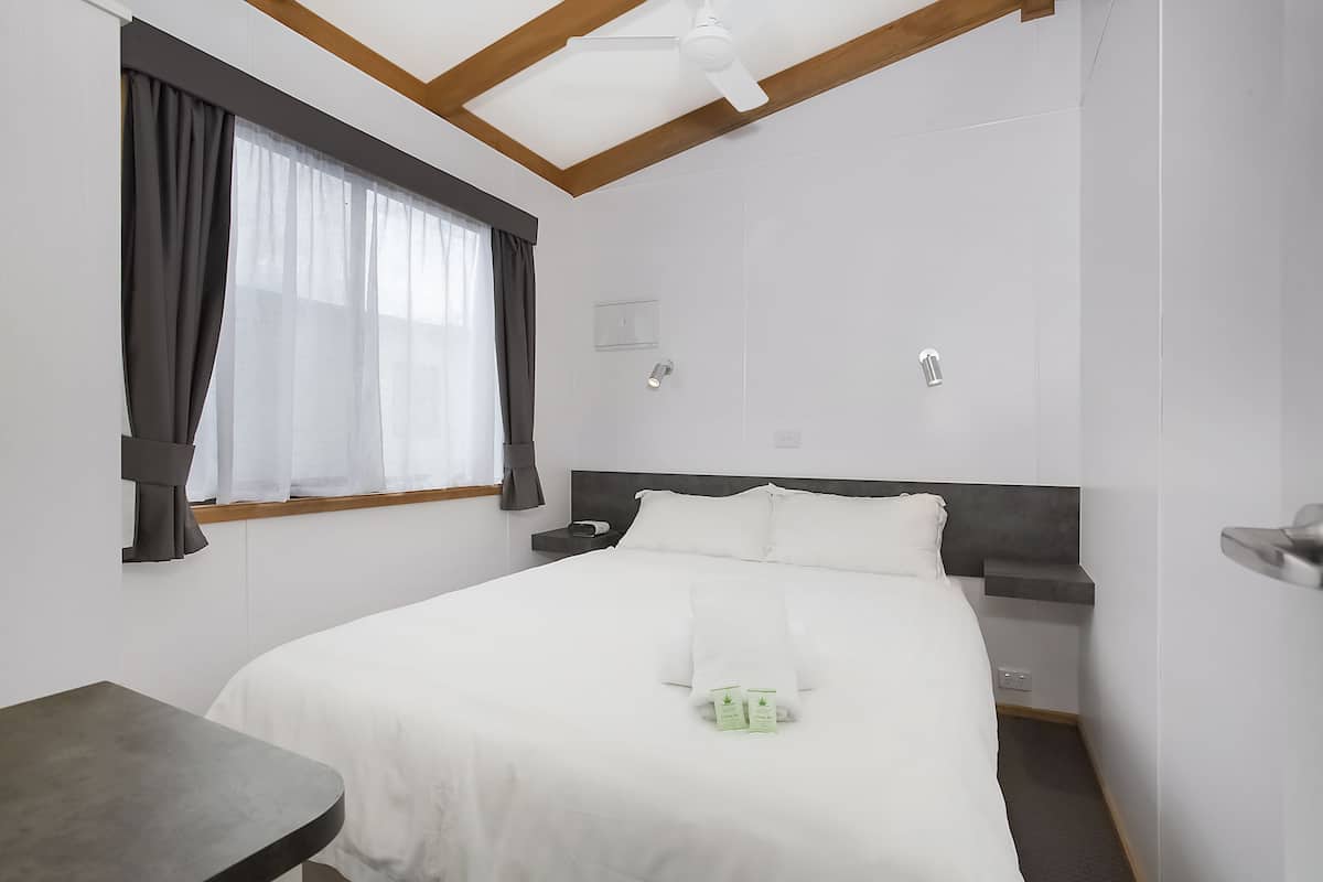 Ein modernes Hotelzimmer mit einem großen Bett, einem Nachttisch, Vorhängen an einem Fenster und einem Deckenventilator.