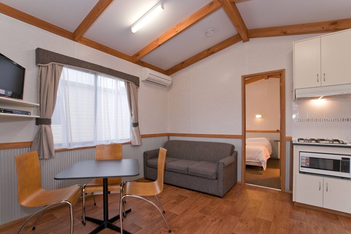 Ein gemütlicher Raum mit Küchenzeile, einer Couch, einem Esstisch mit Stühlen und einem Fernseher.