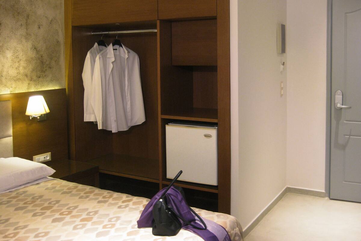 A hotel room with a bed, a wardrobe, a nightstand, a lamp, and a door.