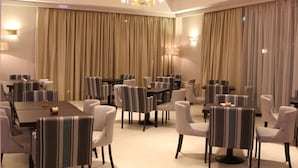 Un comedor de hotel con varias mesas y sillas, cortinas grandes y un candelabro.