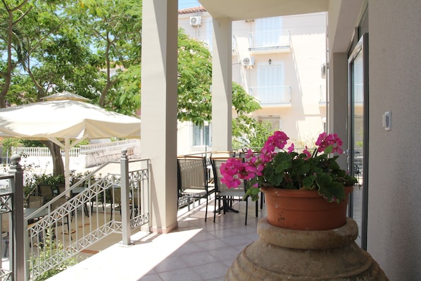 Un balcon avec des sièges d’extérieur, un pot de fleurs orné de fleurs roses et un parasol blanc.