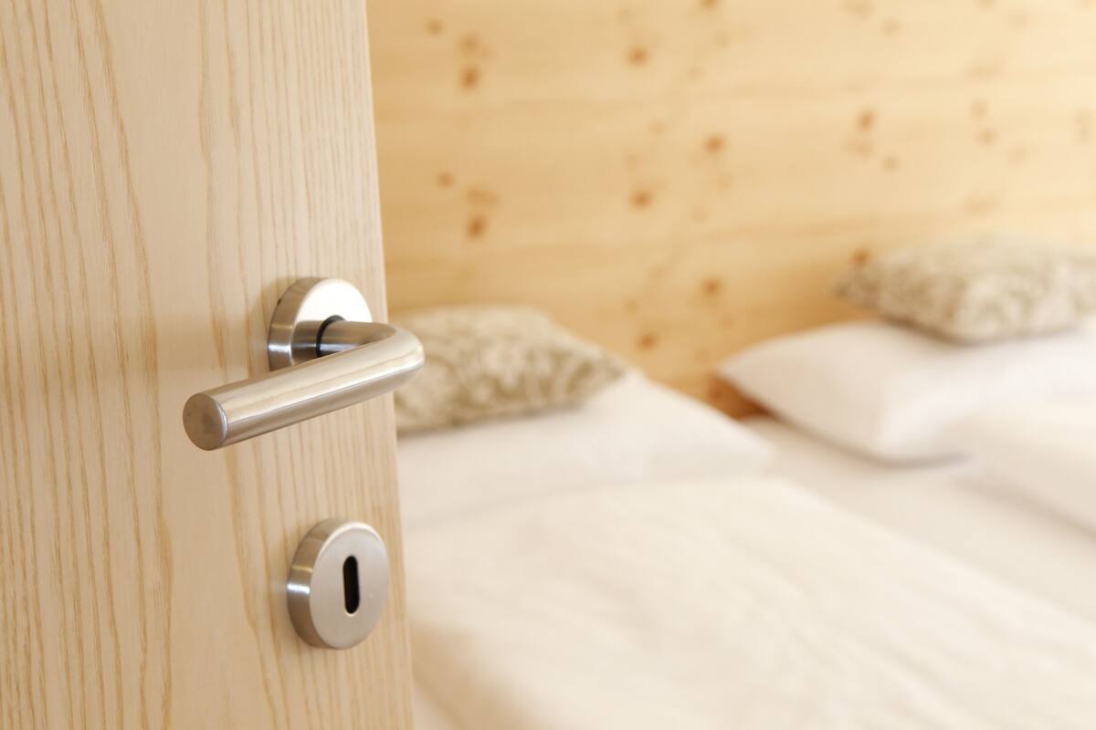 A wooden door with a modern handle and lock, leading to a bed with white bedding and pillows.