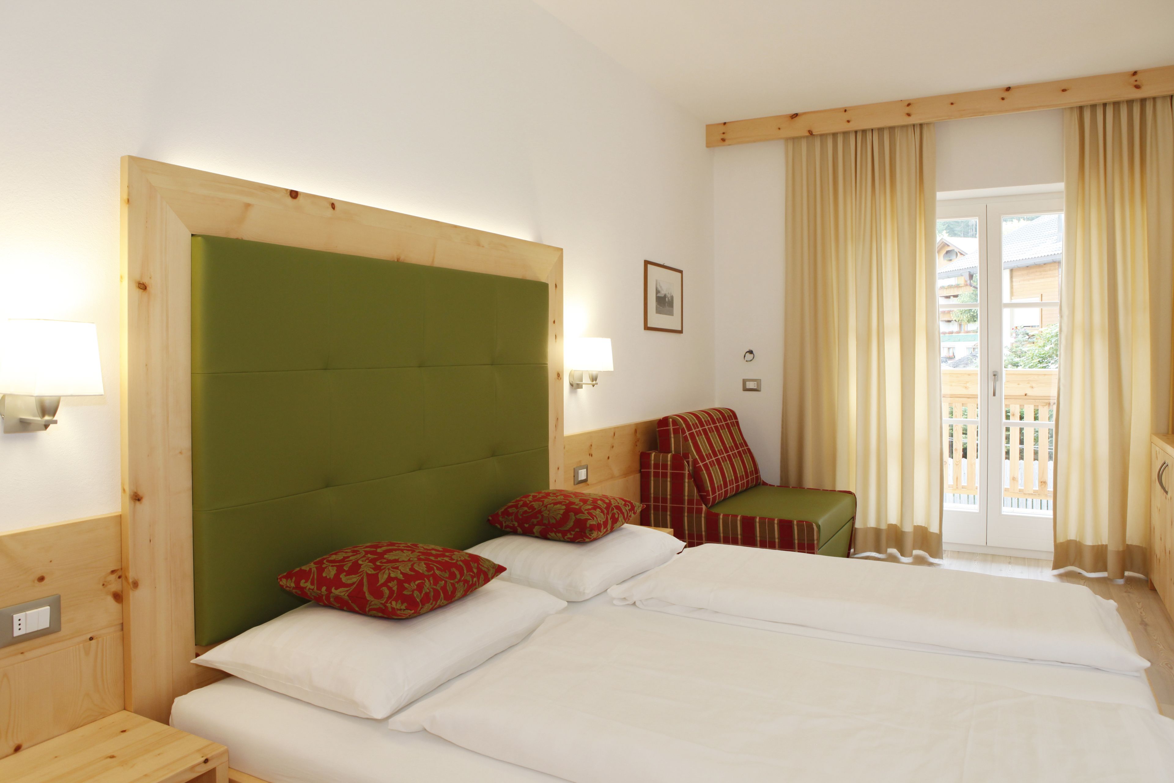 Une chambre d’hôtel avec un grand lit, une tête de lit verte et une vue sur le balcon extérieur.