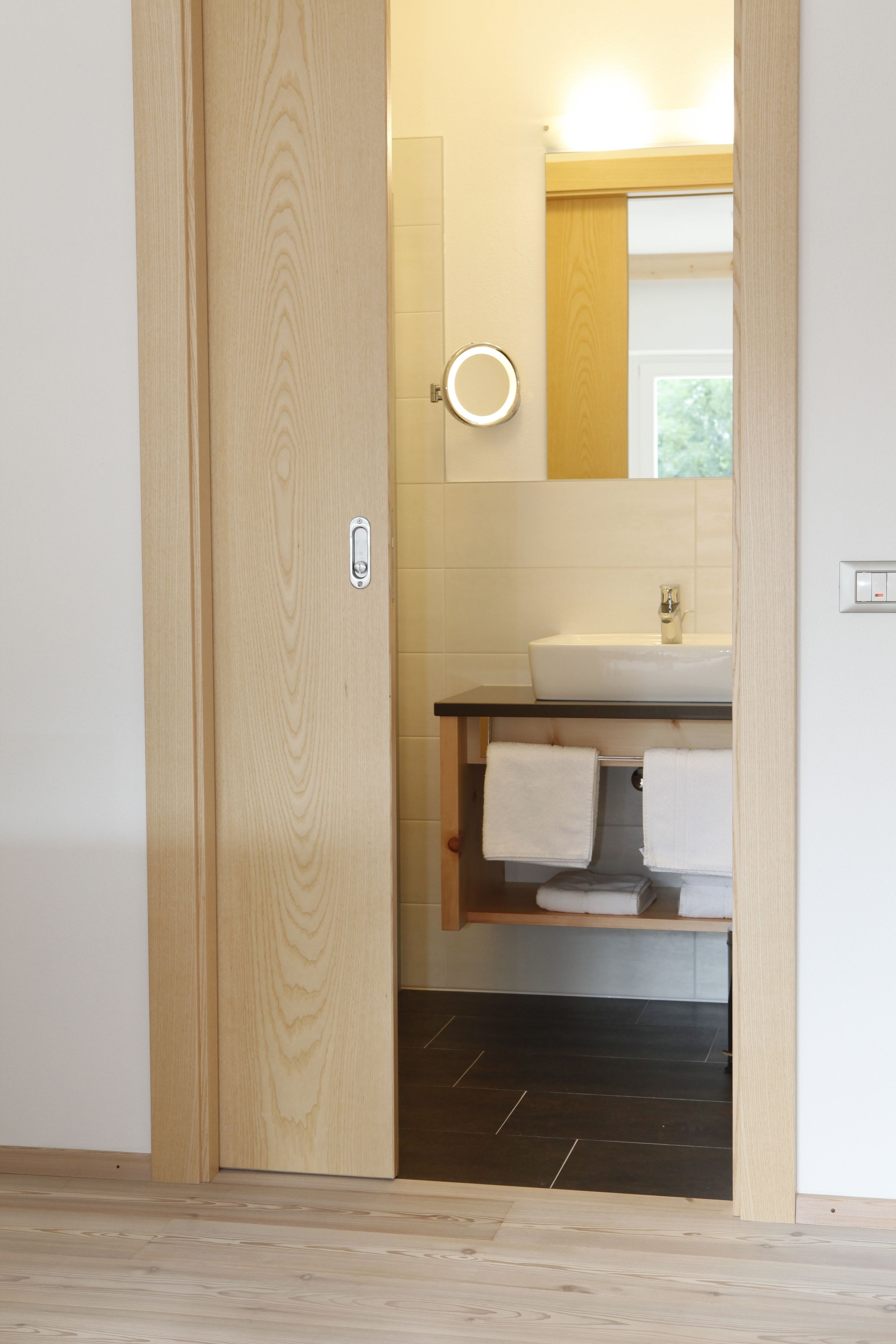 A wooden door leading to a bathroom with a white sink, a mirror, and a towel rack.