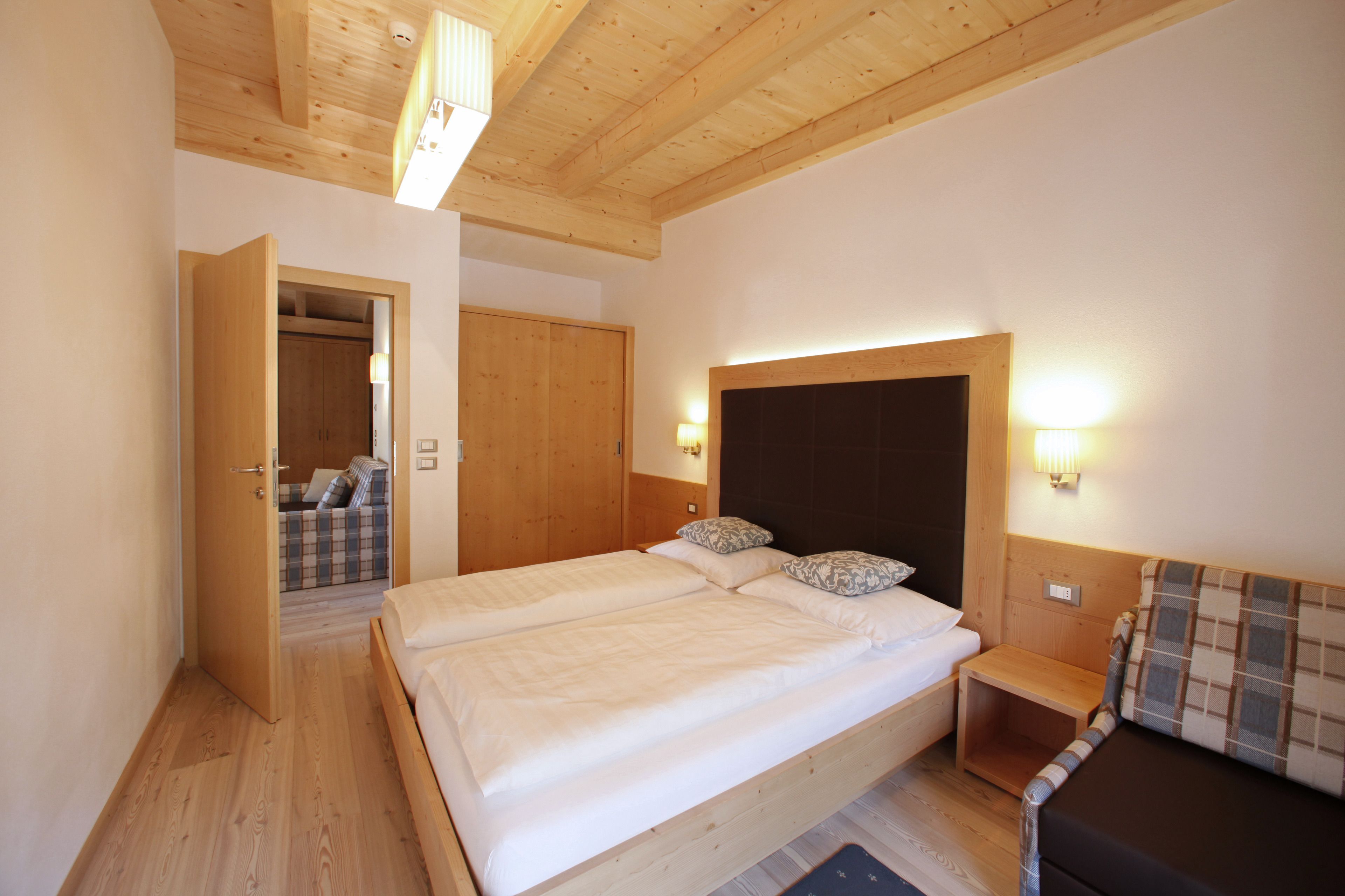 Un dormitorio con dos camas, paredes de madera, techo de madera y un pequeño banco de madera.