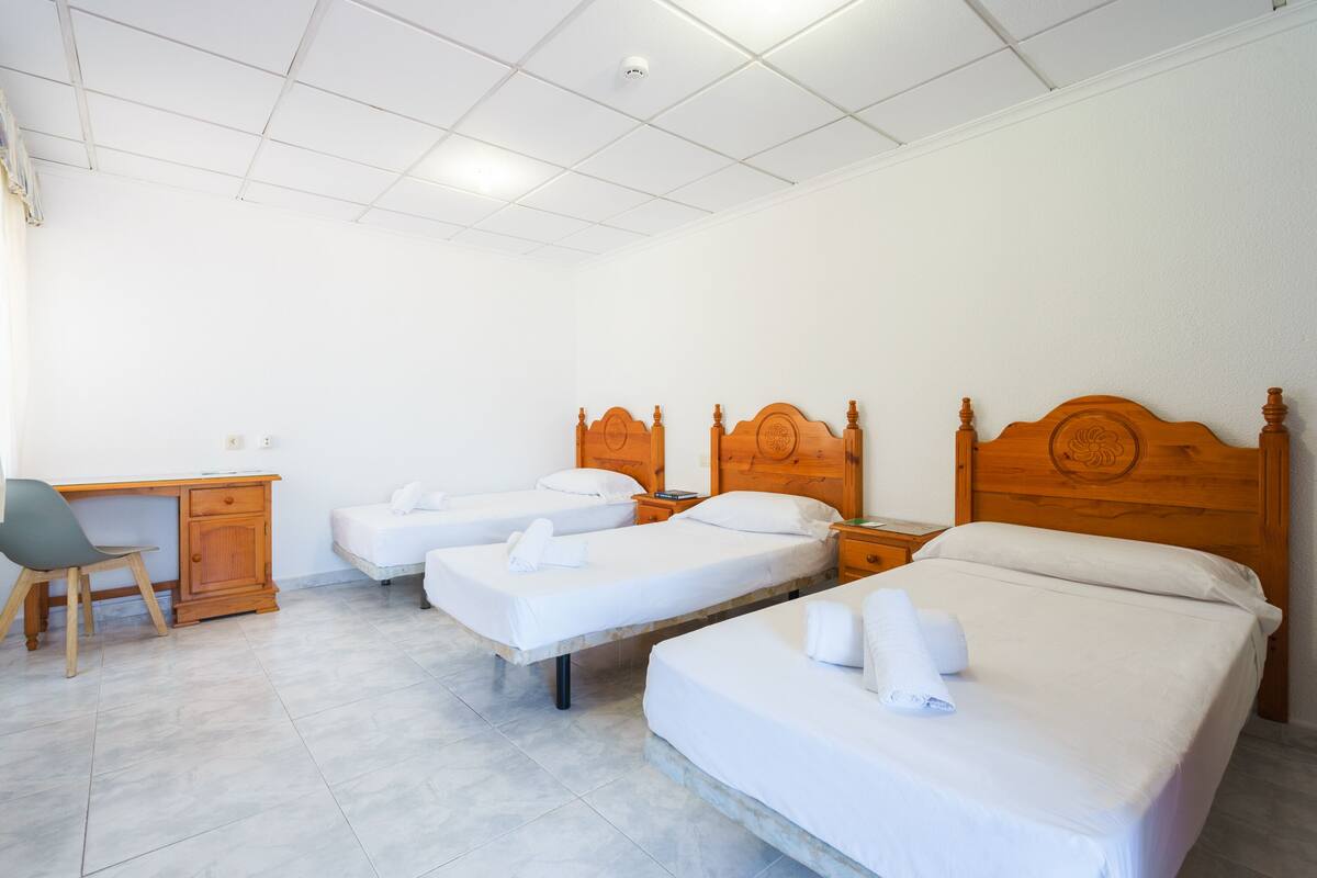A hotel room with three single beds, a wooden desk, and a chair.