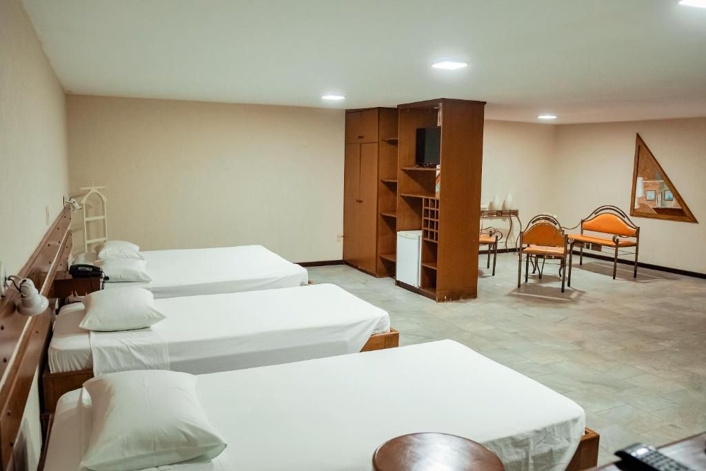 Quarto de hotel com duas camas, uma escrivaninha, uma cadeira e uma mesinha.