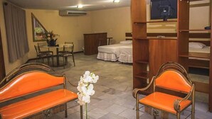 A hotel room with a dining area, a television, a bed, and two orange chairs. - Sakr Hotel (Penapolis)