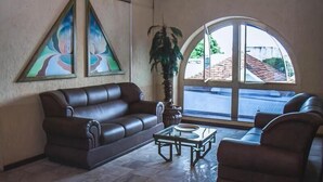 A living room with a brown leather sofa, a glass coffee table, and a large window with a view of a street. - Sakr Hotel (Penapolis)
