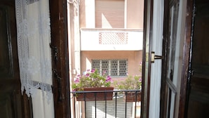 Una vista attraverso una porta aperta, con un balcone, una pianta in vaso fiorita e una ringhiera in metallo.