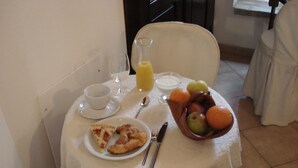 Una tavola imbandita con un piatto di cibo, una ciotola di frutta, un bicchiere di succo d'arancia e una tazza di caffè.