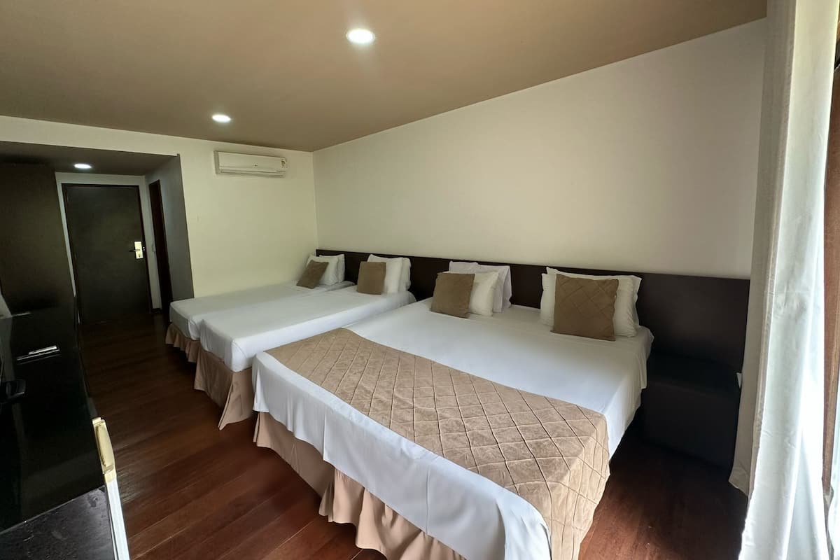Habitación de hotel con dos camas, suelo de madera oscura, paredes blancas e iluminación empotrada en el techo.