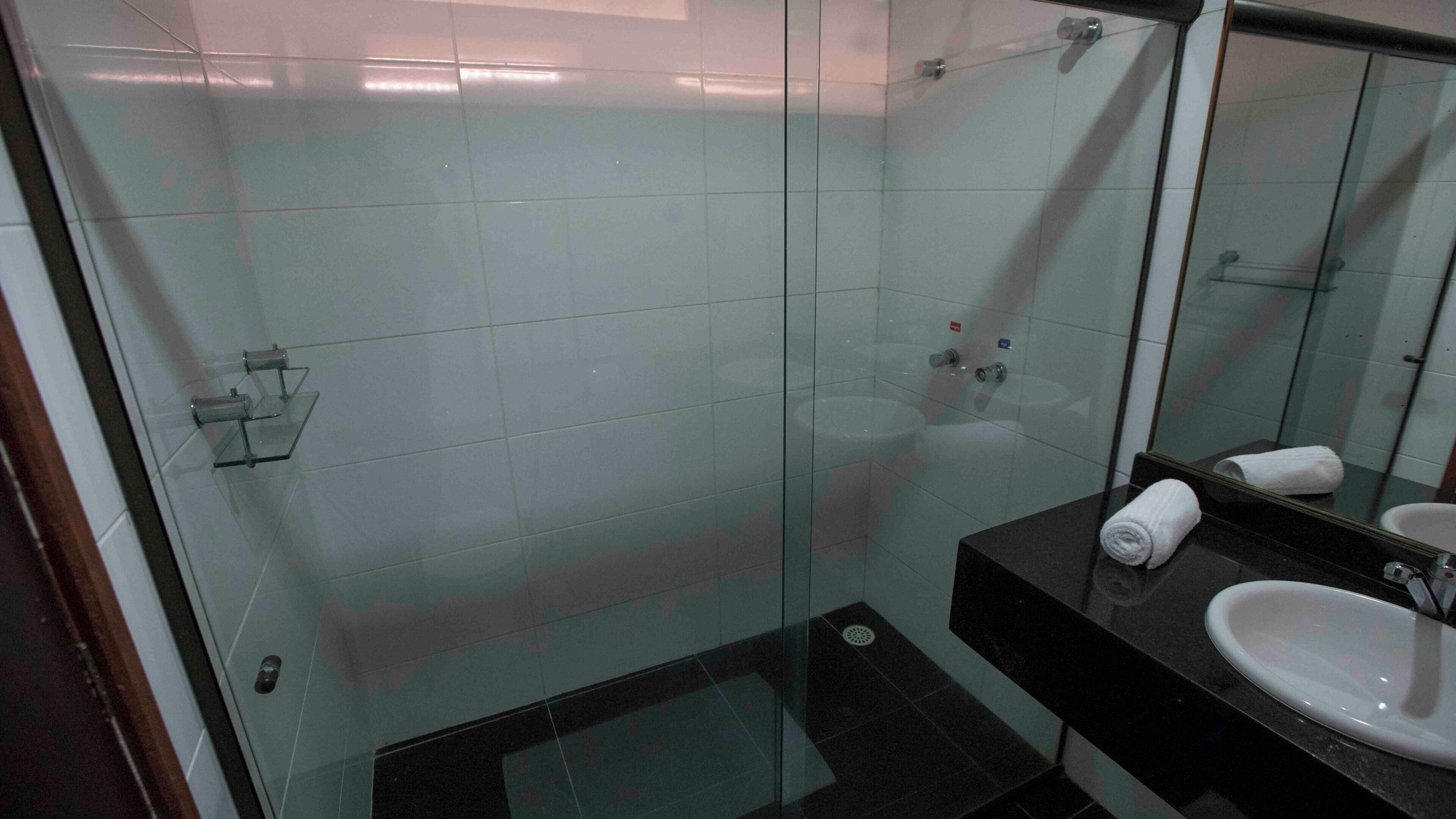A modern bathroom with a glass shower enclosure, a black sink, and a mirror reflecting the space.