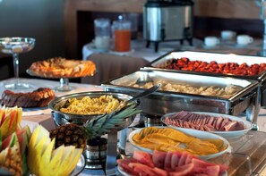 Un bufé con diversas opciones de comida, entre ellas frutas, verduras y carnes.
