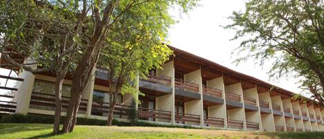 A multi-story building with balconies, surrounded by trees and grass.