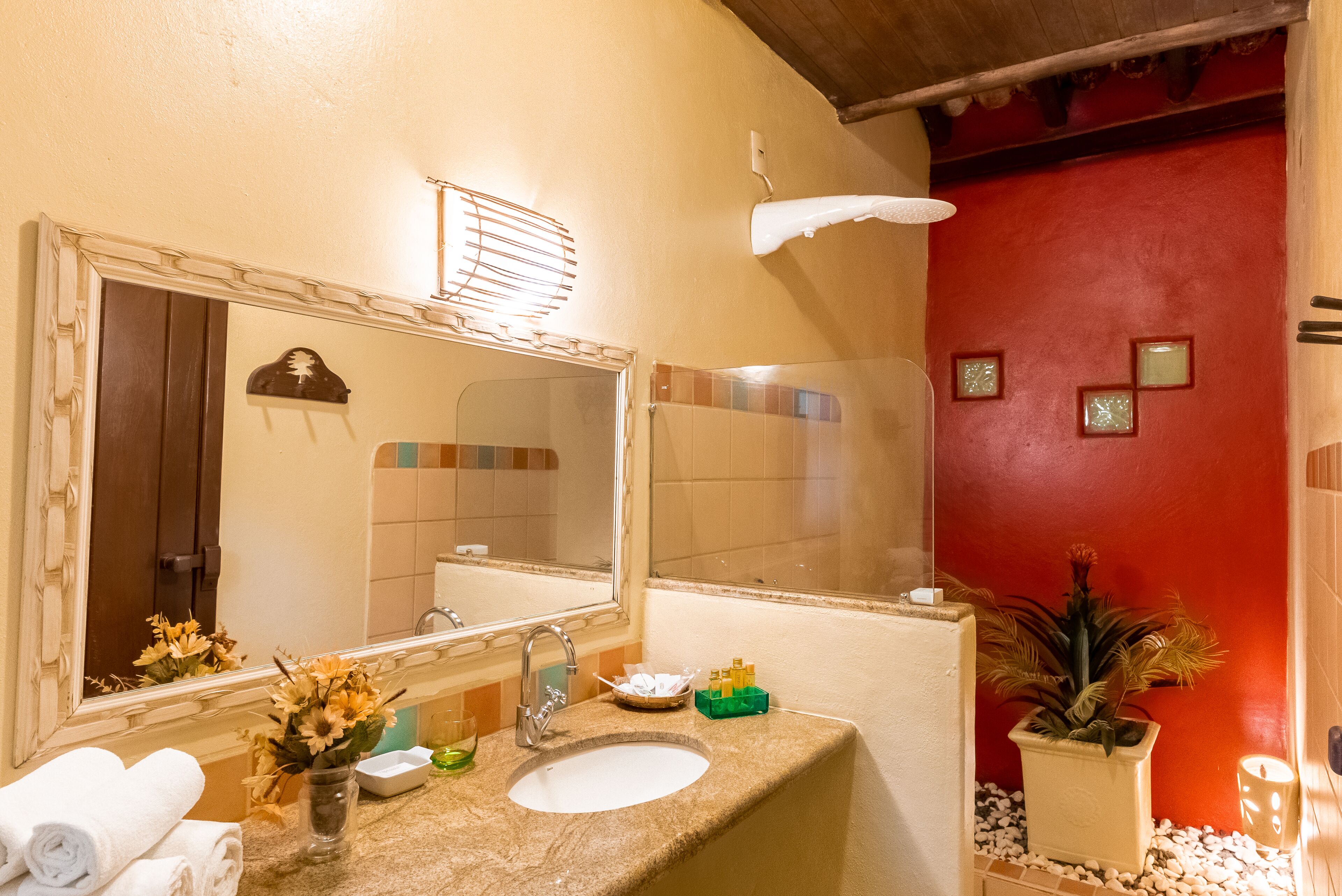 Un baño con un lavamanos blanco, un espejo grande, un perchero y una planta en maceta.