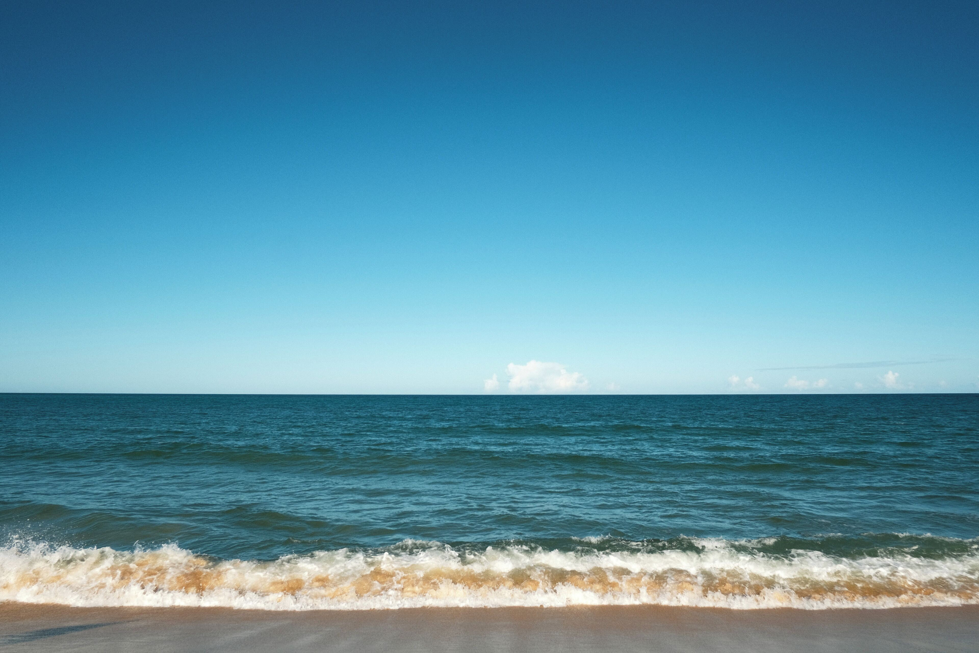 A beach with waves gently lapping at the shore under a clear blue sky.