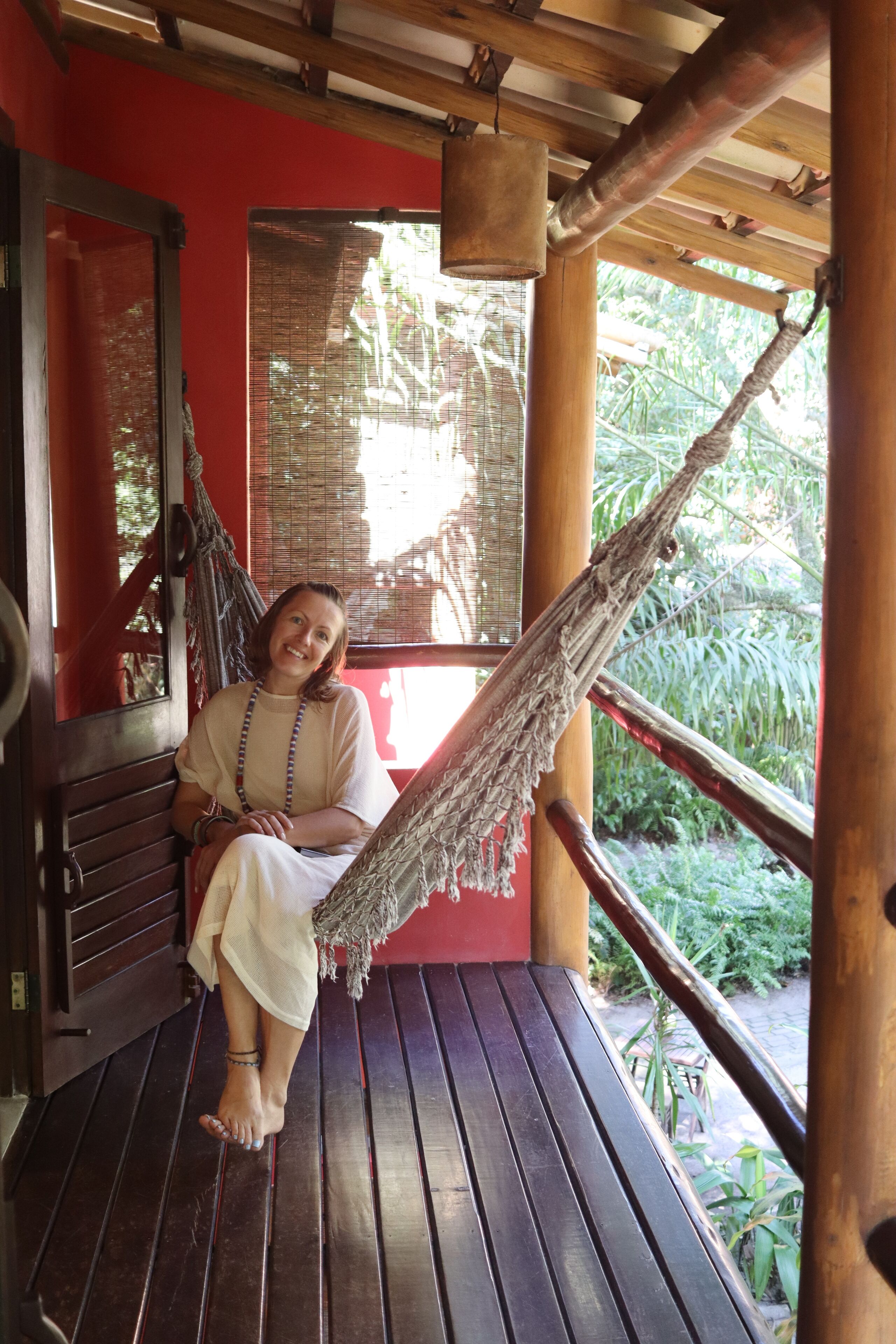 A person sitting on a wooden bench under a wooden structure with a hammock.