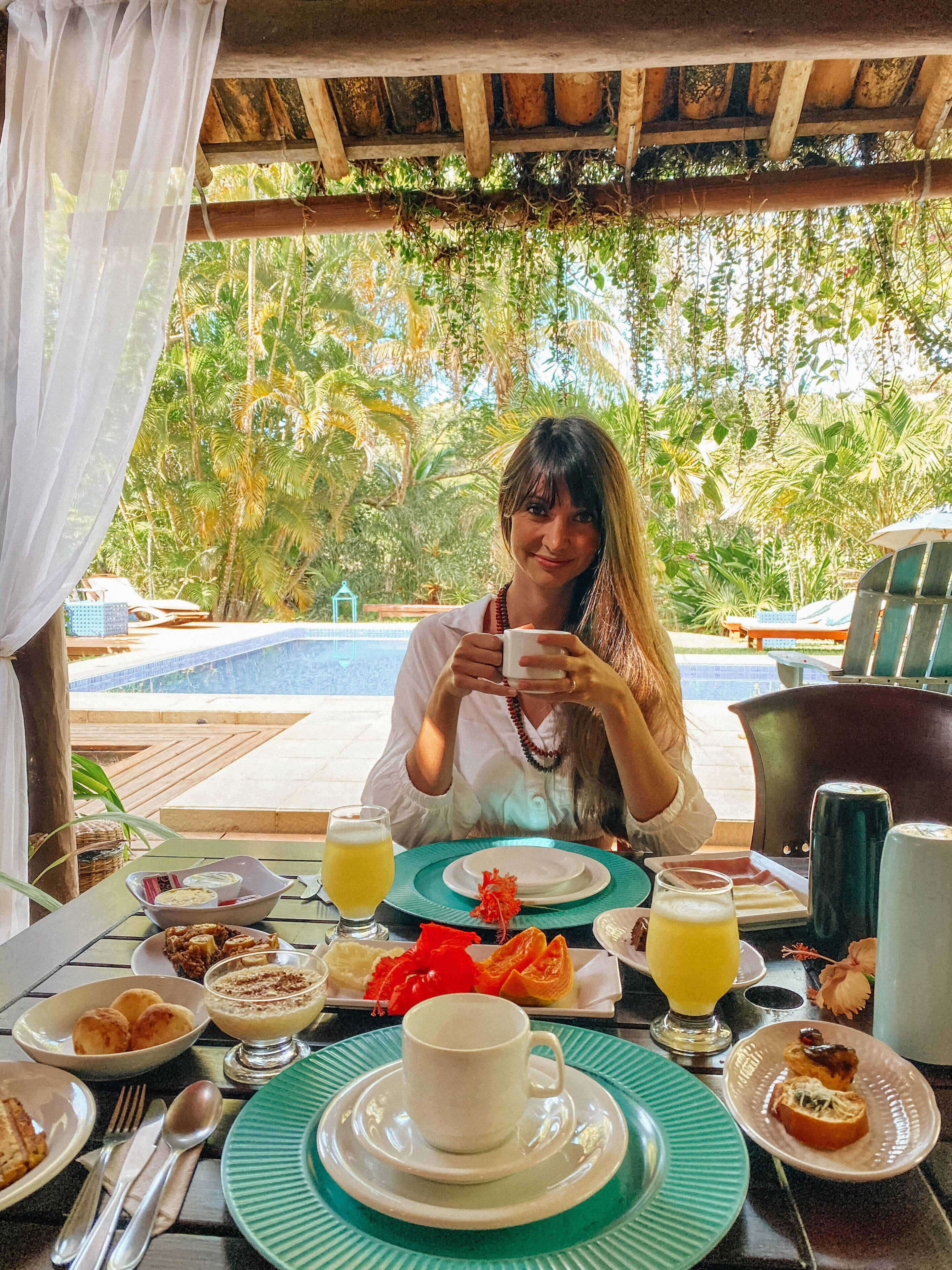 A dining table set with breakfast items, a pool in the background, and lush greenery.
