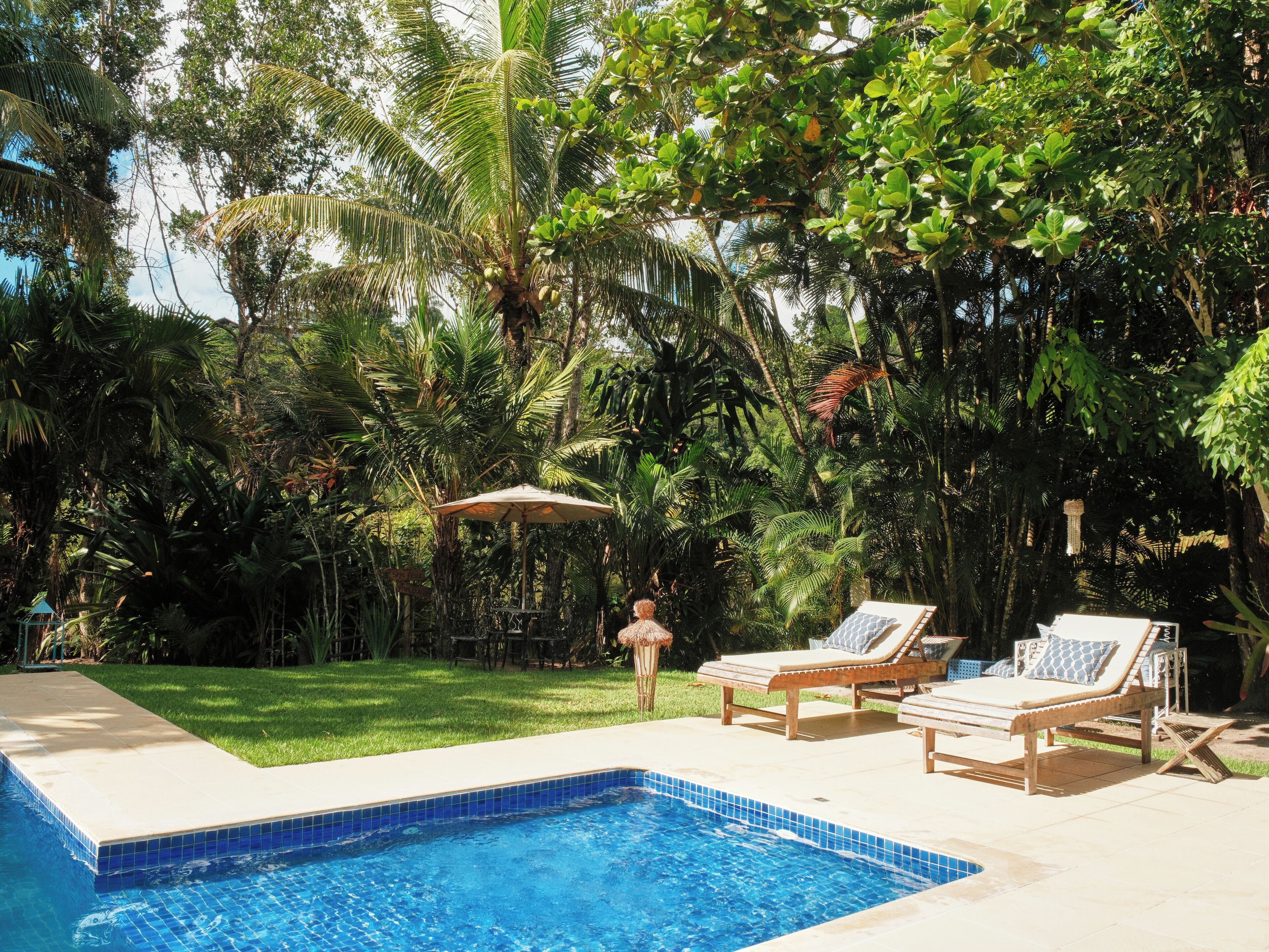 A swimming pool with lounge chairs and a table, surrounded by lush greenery and palm trees.