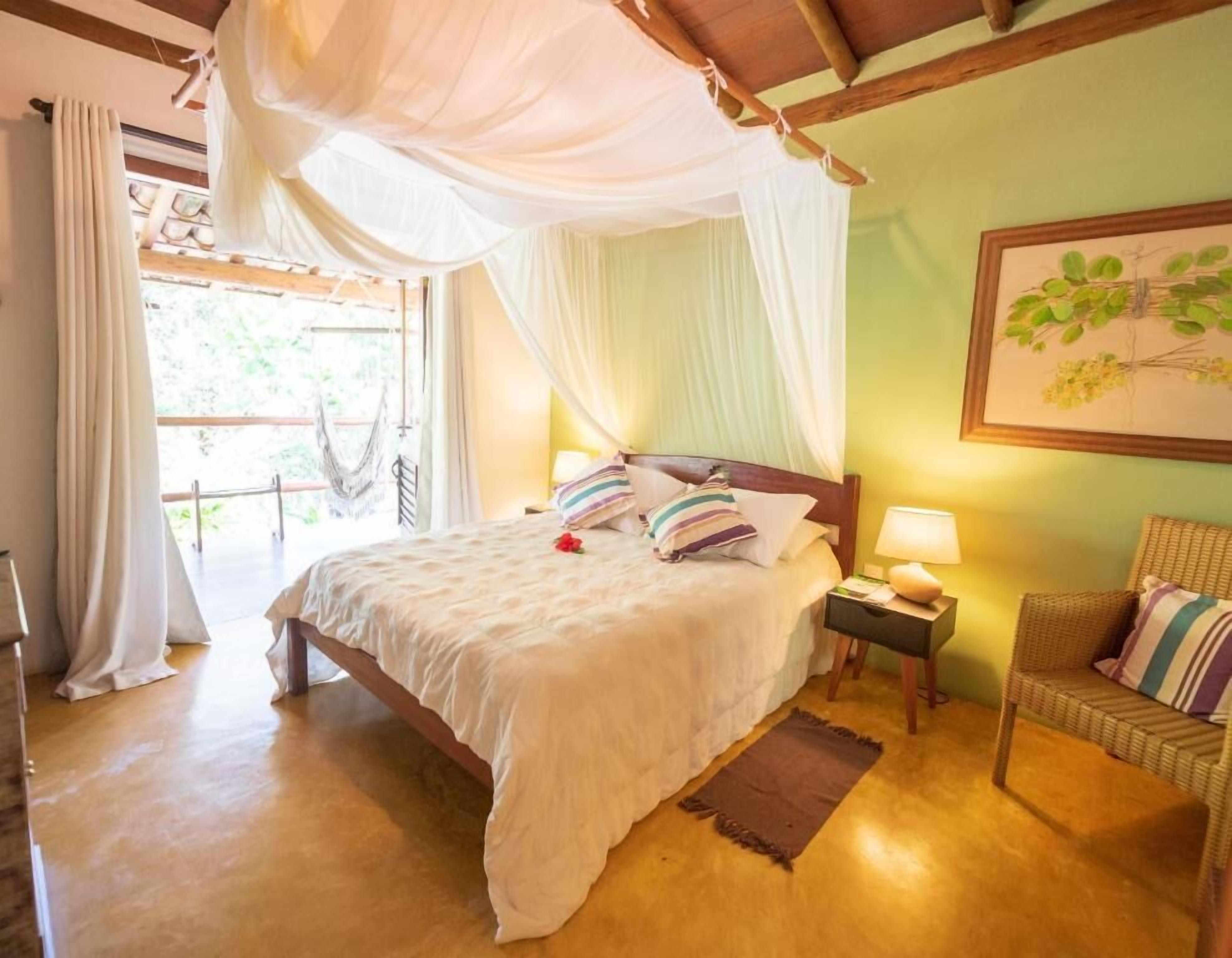 A bedroom with a bed, a nightstand, a chair, and a window with curtains.