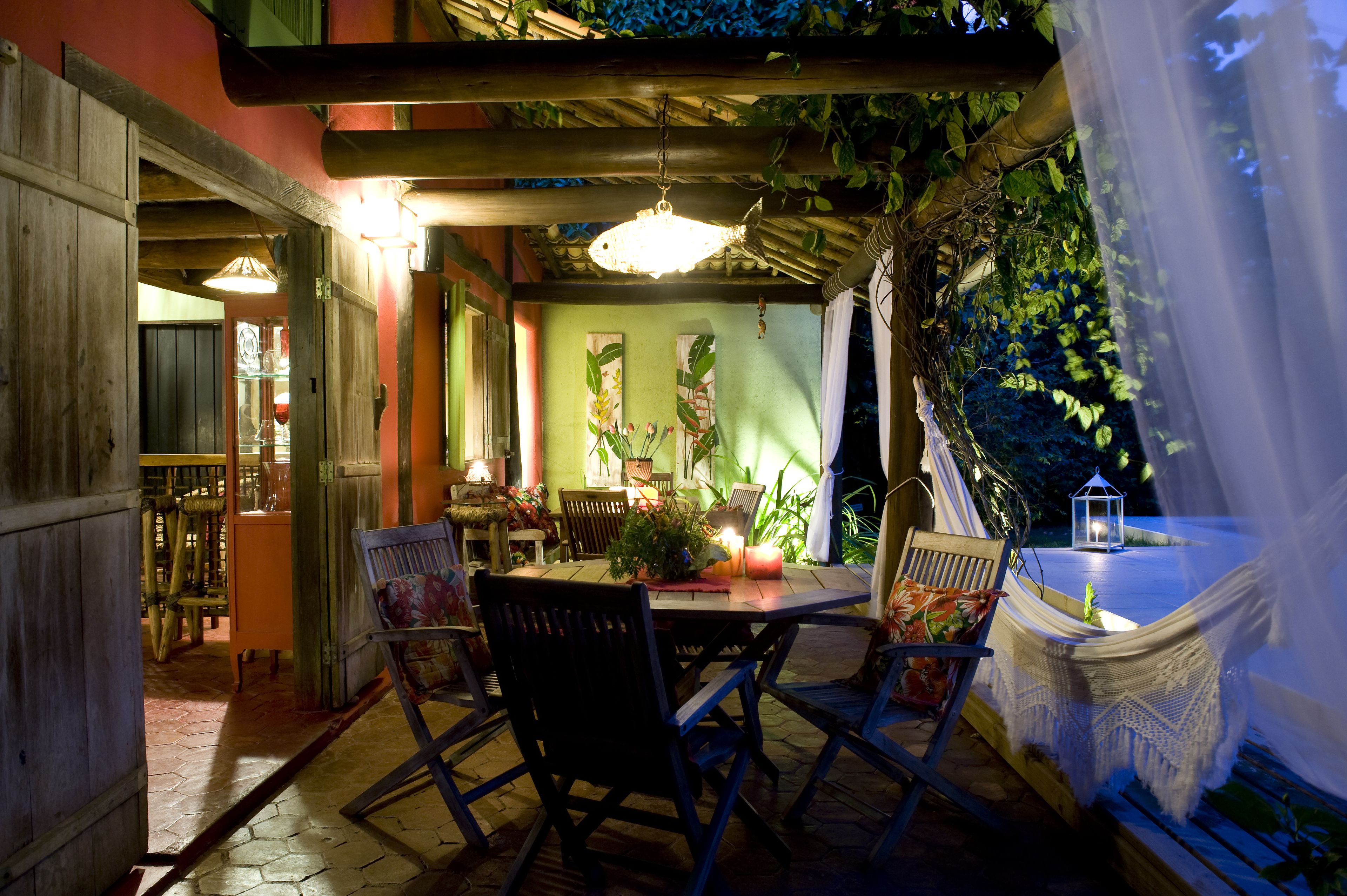 Un área de comedor al aire libre con una mesa y sillas de madera, rodeada de plantas y un colgante luminoso.