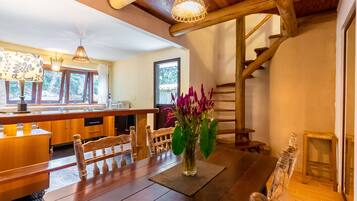 A wooden dining table with a vase of flowers, a wooden bench, and a staircase with wooden railings.