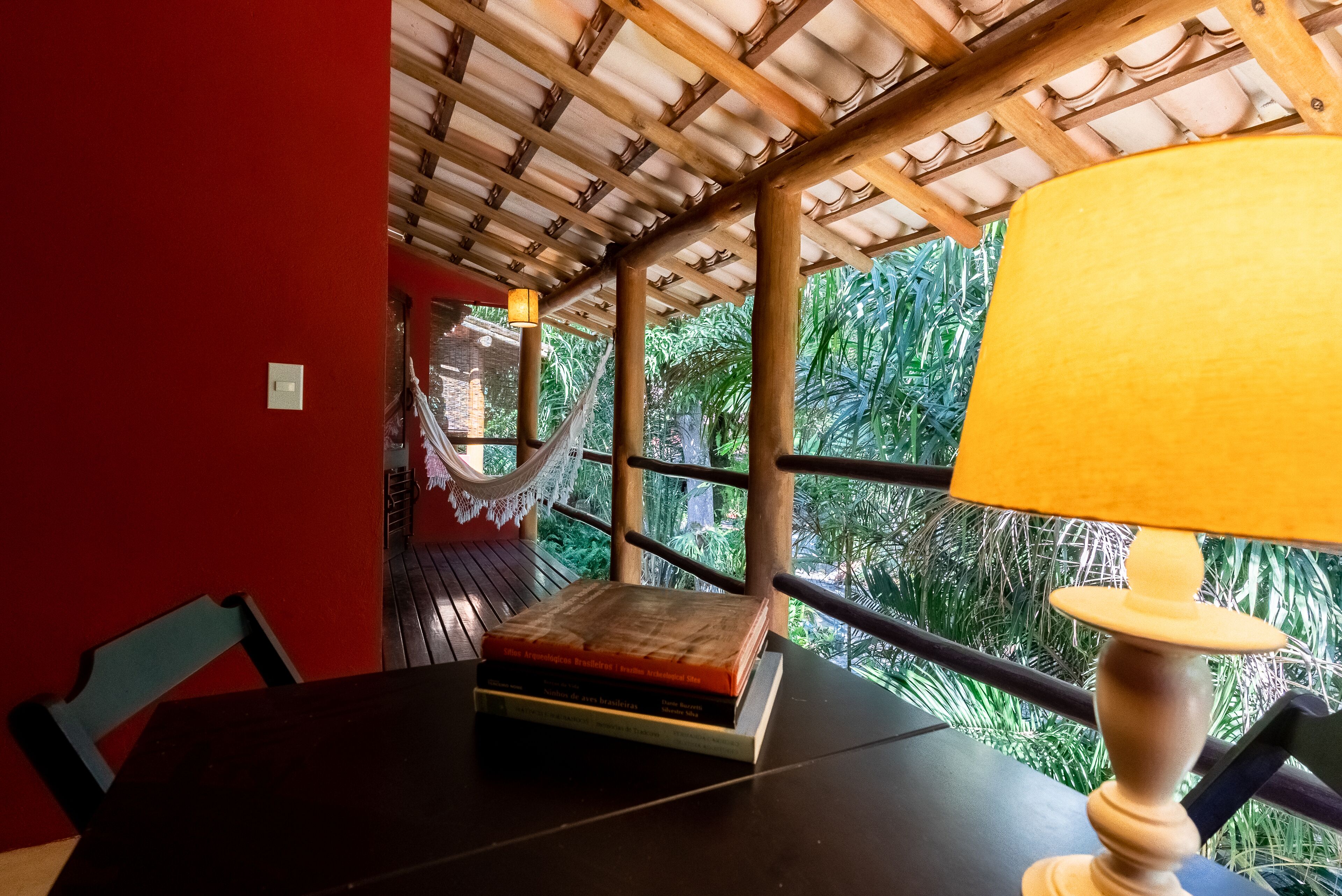 A room with a wooden ceiling, a table with a lamp, and a view of greenery outside.