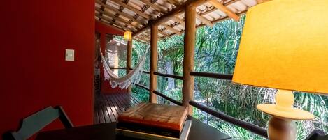A room with a wooden ceiling, a table with a lamp, and a view of greenery outside.