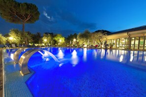 A large indoor swimming pool with a blue tint, surrounded by lounge chairs and trees. - Terme Petrarca (Montegrotto Terme)