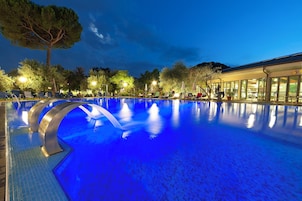 Una amplia piscina interior con un tono azul, rodeada de sillas de descanso y árboles.