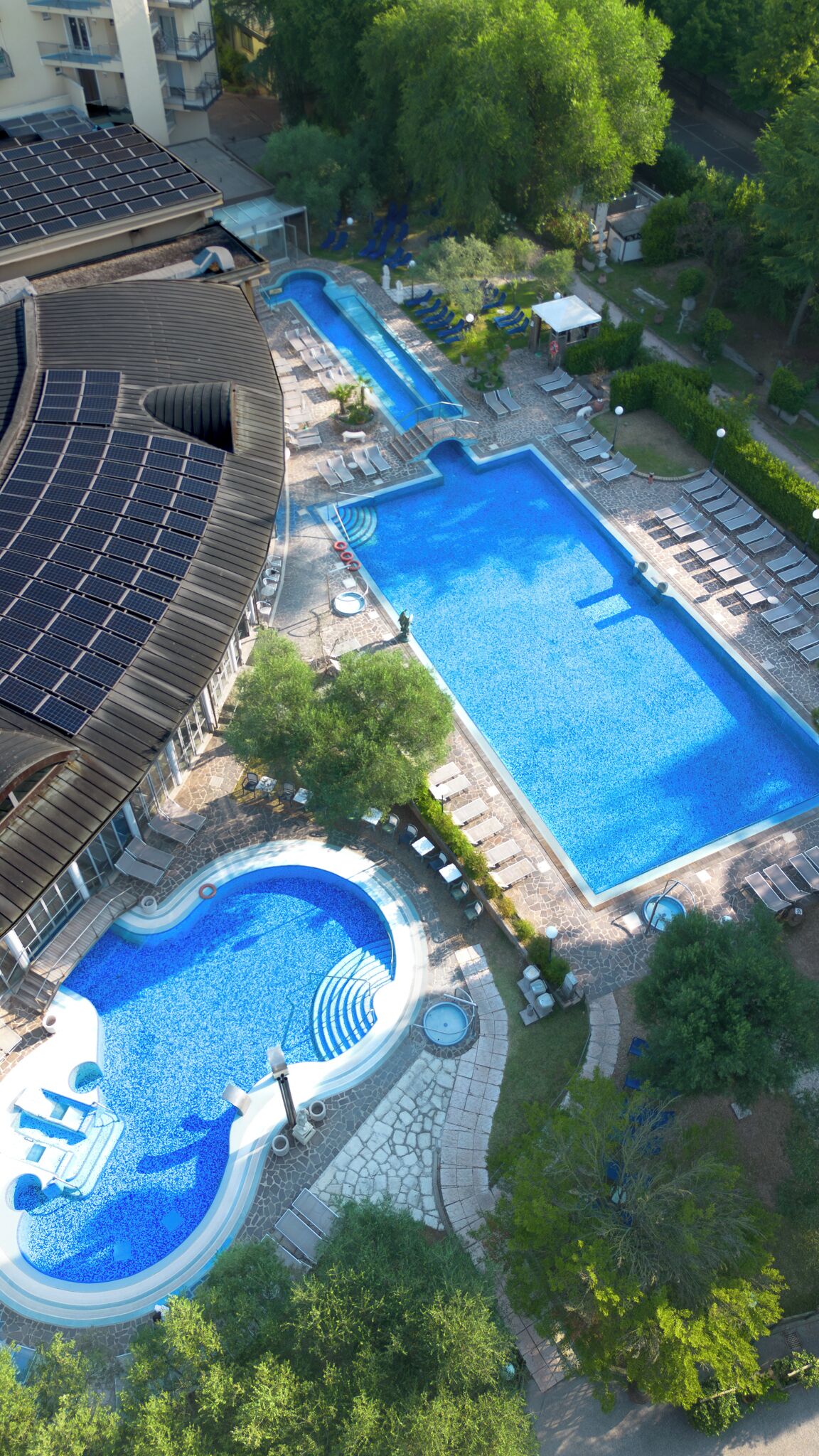 Una piscina en la azotea con un jacuzzi circular, una piscina rectangular y zonas de descanso con tumbonas.