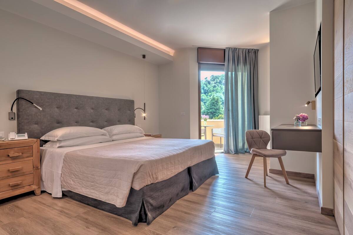 A modern bedroom with a large bed, bedside tables, a desk, and a chair.