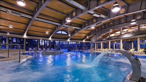 Una piscina interior con varias pistas, iluminación en el techo y vistas al exterior a través de amplios ventanales.