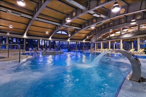 Una piscina interior con varias pistas, iluminación en el techo y vistas al exterior a través de amplios ventanales.