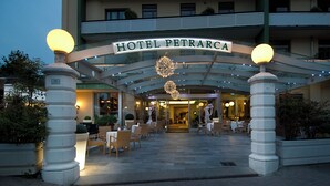 La entrada del Hotel Petrarca con un letrero, zona de estar al aire libre e iluminación decorativa.