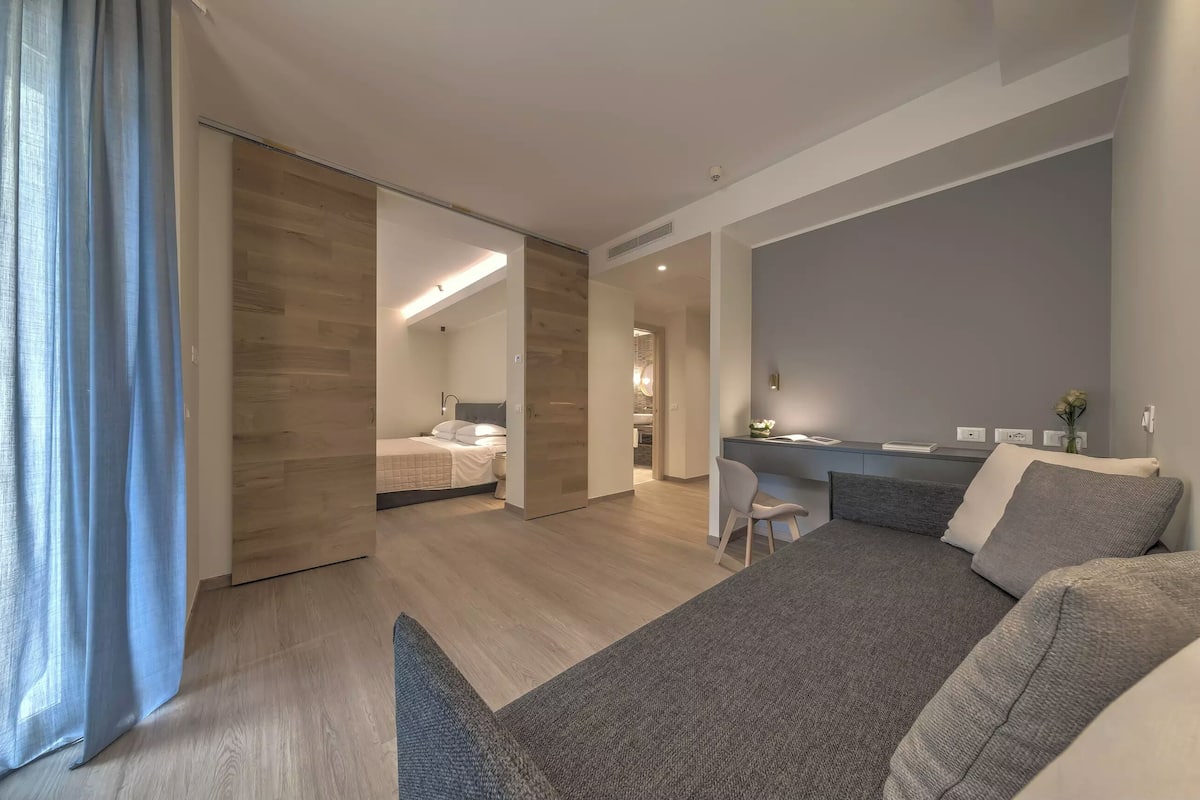 A modern hotel room with a large bed, a desk, and a sliding door leading to a bathroom.
