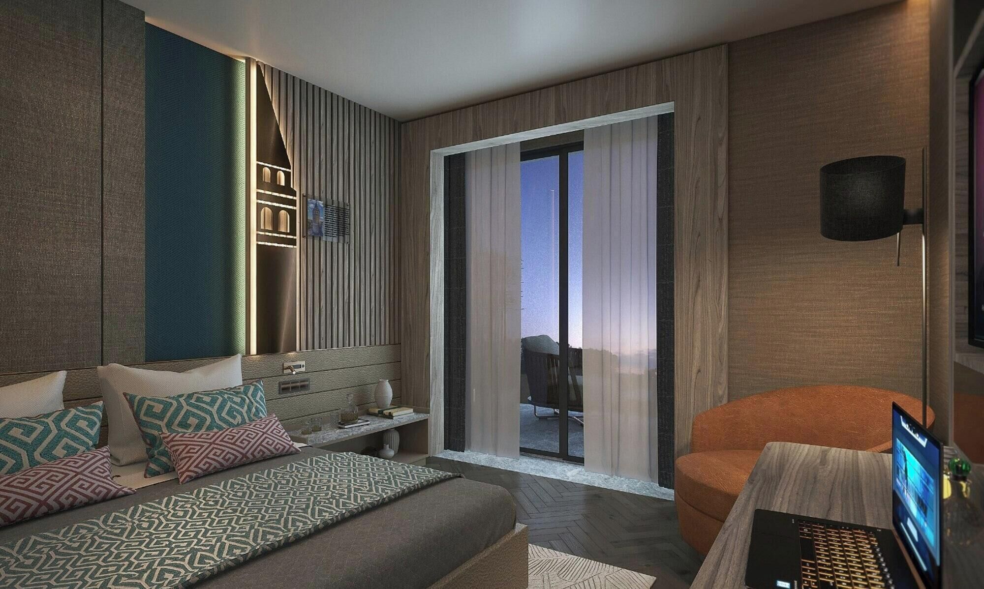 Moderni hotellihuone, jossa on sänky, oleskelualue, kannettava tietokone ja näkymä liukuoven kautta.